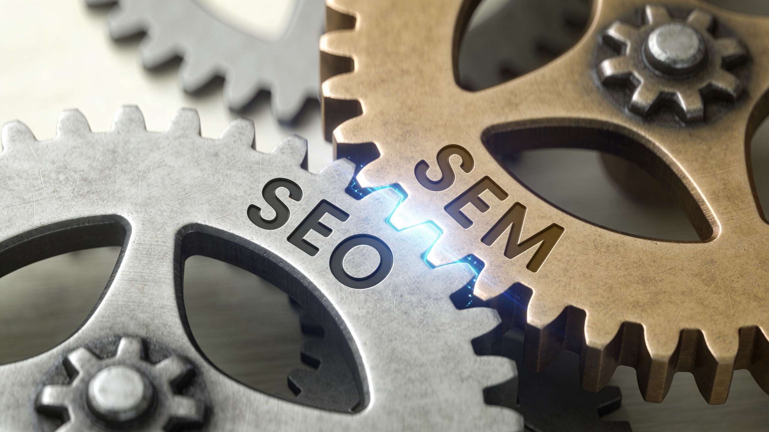 Interlocking silver and gold gears showing the text SEO and SEM connected by a glowing electric spark.