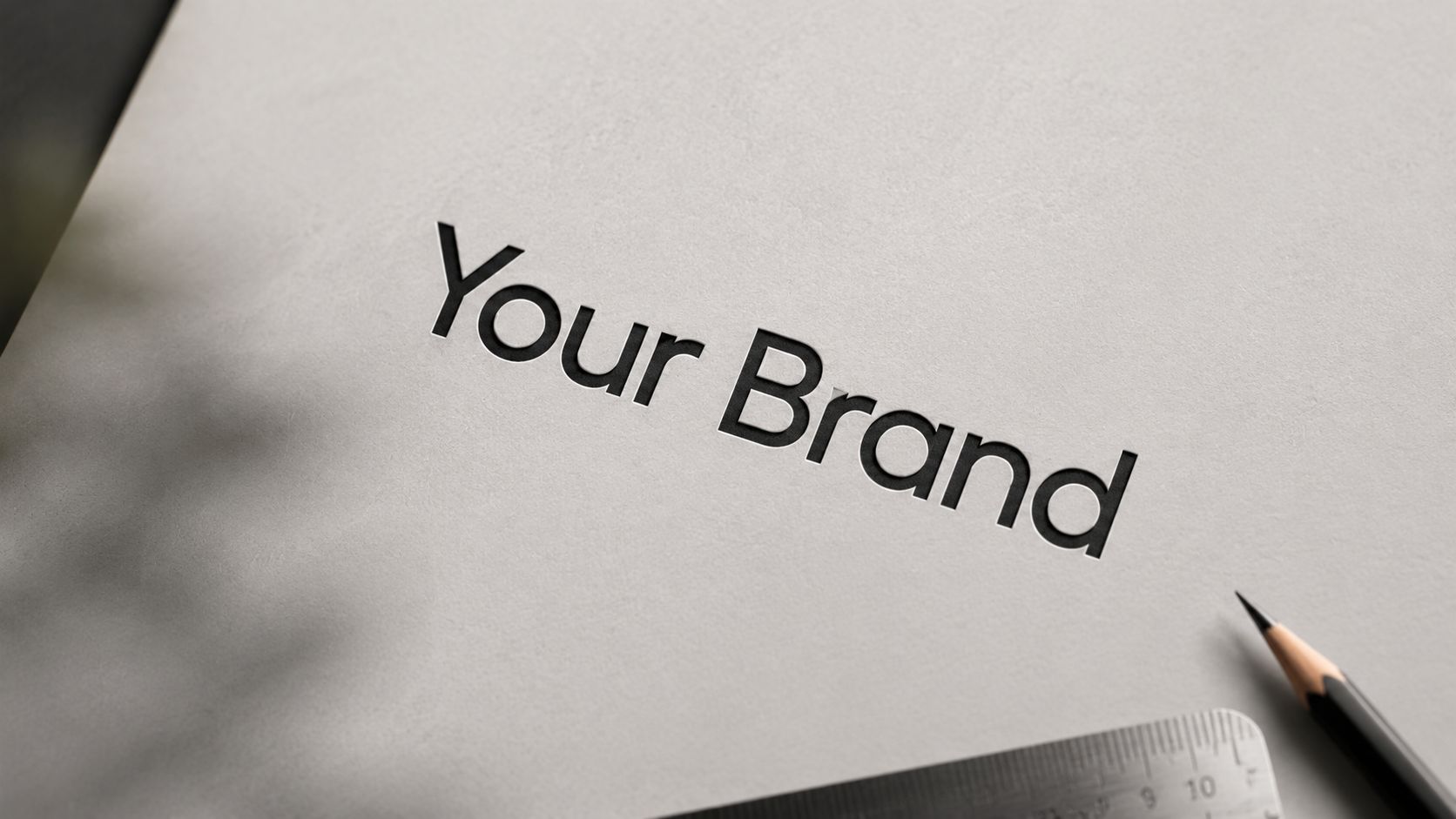 A professional mockup featuring the text Your Brand embossed on light gray paper with a pencil and ruler.